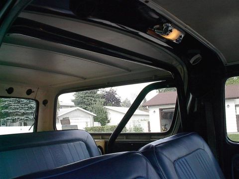 1979 Ford Bronco - The interior of a 1978 Ford Bronco, showing the rear bench seat and a roll cage, with a view of houses and trees through the windows.