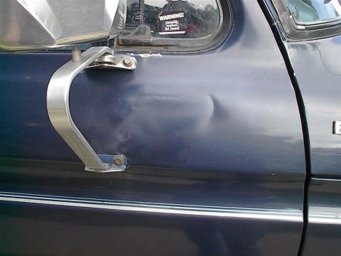 1979 Ford Bronco - This photo shows a dented door panel on a vehicle, with a warning sticker on the window.