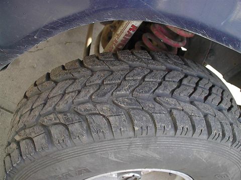 1979 Ford Bronco - A close-up view of a vehicle's tire and suspension system, showing a red coil spring and a shock absorber.