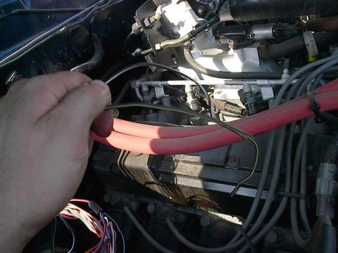 1979 Ford Bronco - Close-up of an engine bay with a hand manipulating wires near the fuel injection system.