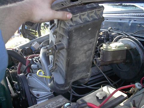 1979 Ford Bronco - Close-up of a vehicle's engine bay as someone removes the air intake assembly.