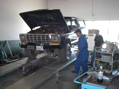 1979 Ford Bronco - A mechanic inspects the engine of a 1978 Ford Bronco, which is raised on a service lift in a garage.