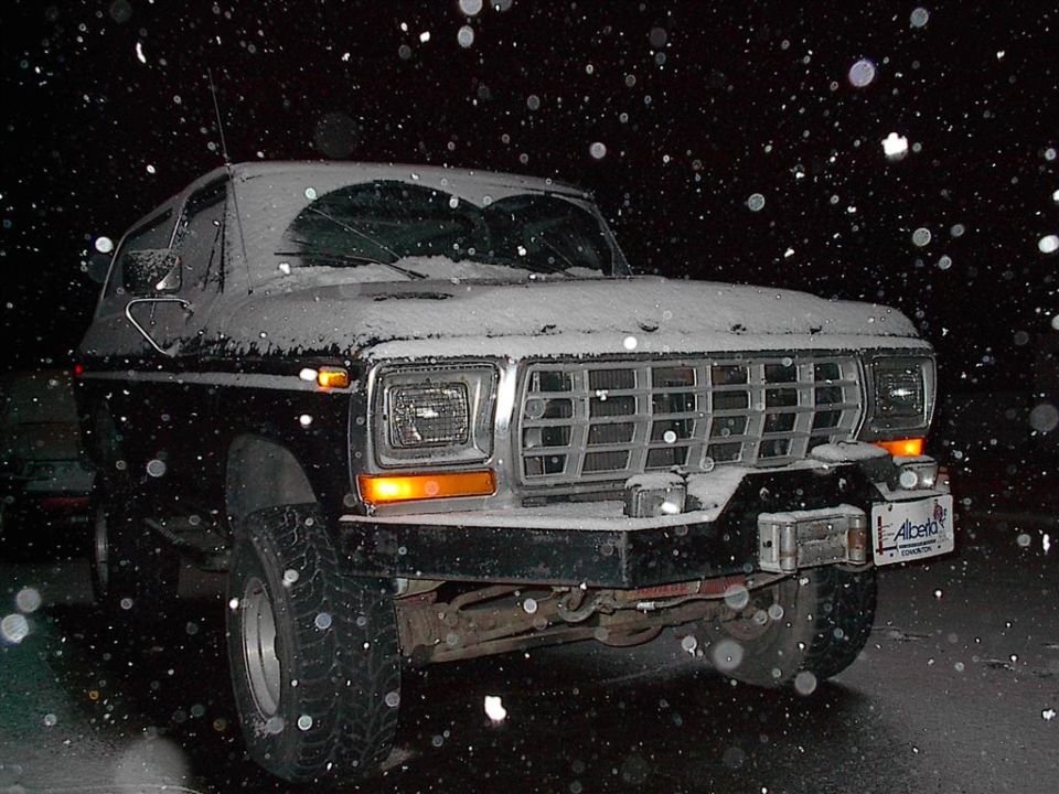 1978 Ford Bronco with snow on its hood and windshield, parked at night