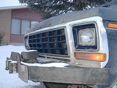 1979 Ford Bronco - The front grille and bumper of a Ford truck are visible in this close-up shot, with snow on the ground.