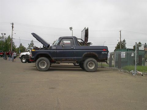 1979 Ford Bronco - A dark blue Ford Bronco is parked with its hood open, next to another vehicle, with a dumpster in the background.