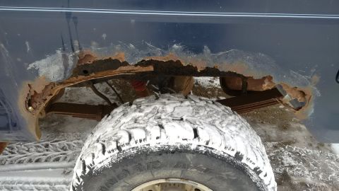 1979 Ford Bronco - The underside of a dark blue vehicle shows significant rust damage around the rear wheel well, which is covered in snow.