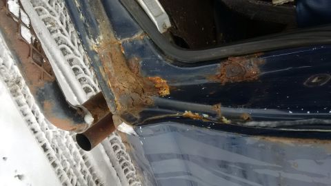 1979 Ford Bronco - Close-up of severe rust on a vehicle's door frame and exhaust pipe in a snowy environment.