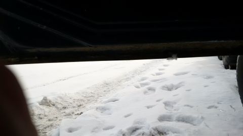 1979 Ford Bronco - A low-angle shot shows the undercarriage of a vehicle with snow and footprints on the ground.