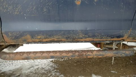 1979 Ford Bronco - The side of a dark blue vehicle shows significant rust on the running boards and lower body panels.
