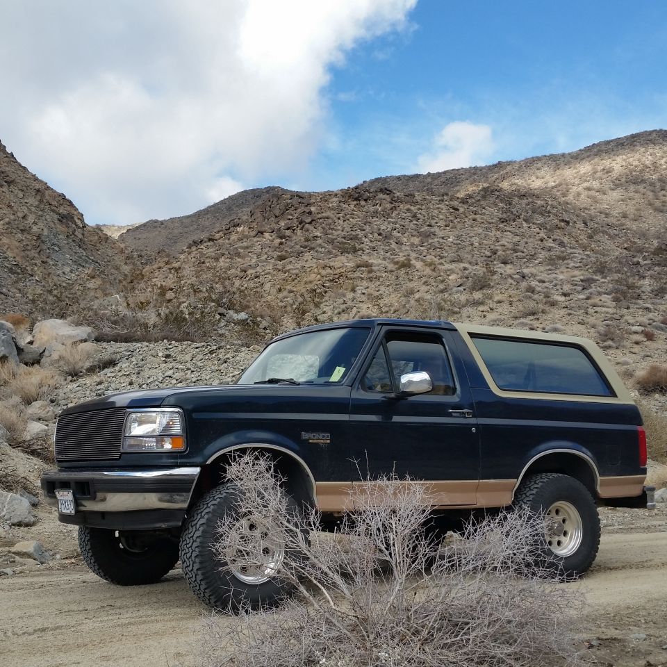 Dark blue Ford Bronco with tan top parked on dirt road in desert landscape