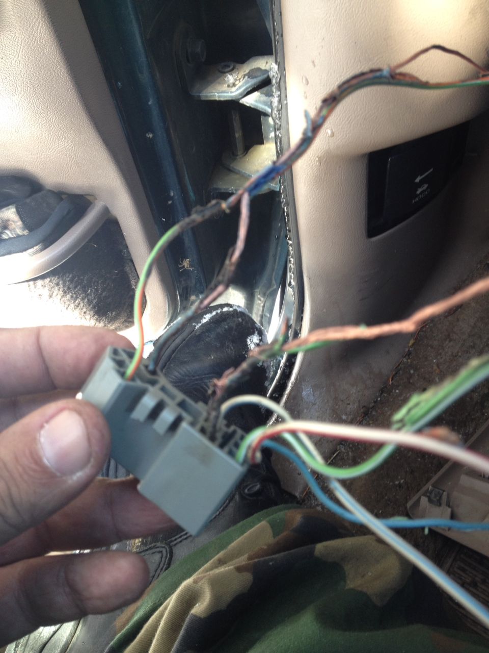 Hand holding gray wiring harness connector with frayed wires