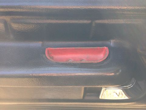 1979 Ford Bronco - Interior shot of a vehicle's door panel, a red reflector and a chrome pull handle.