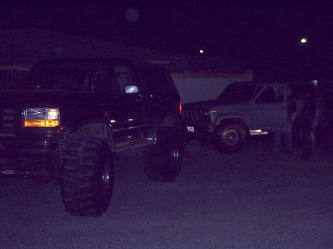 1996 Ford Bronco - Two SUVs are parked at night, one black and heavily modified, the other a lighter color.