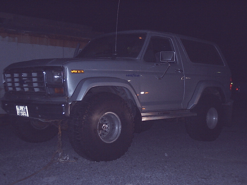 Silver two-door lifted Ford Bronco SUV at night, front three-quarter view with big off-road tires