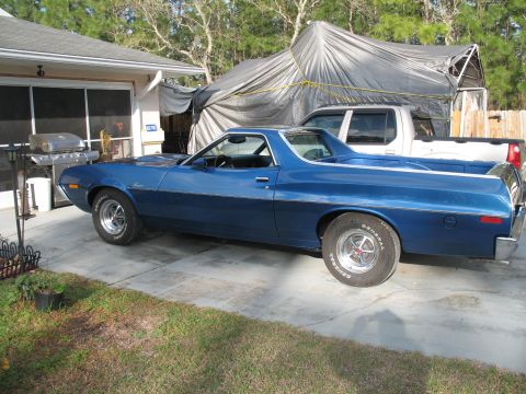 1972 Ford Ranchero - A blue 1972 Ford Ranchero is parked in a driveway, with a white pickup truck visible behind it under a large tarp.