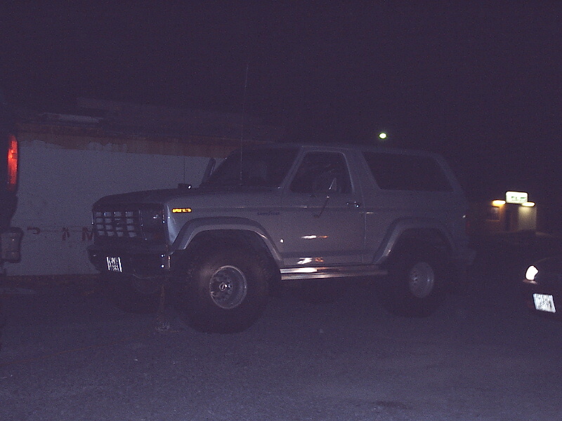 Silver two-door Ford Bronco SUV at night, front 3/4 view, lifted with off-road tires