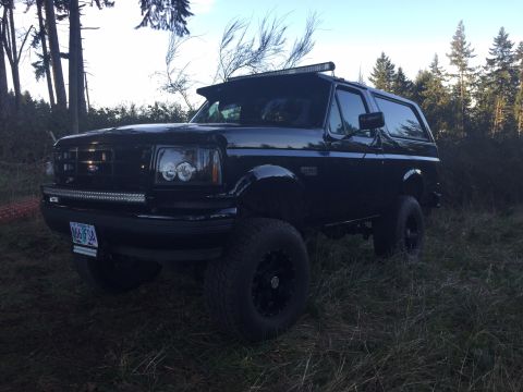 1992 Ford Bronco - This black 1992 Ford Bronco is parked off-road with a light bar mounted above the windshield.