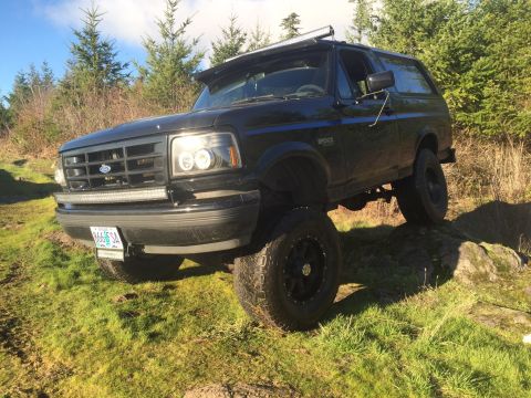 1992 Ford Bronco - This black 1992 Ford Bronco is equipped with auxiliary lighting and large off-road tires, shown navigating rocky ground.