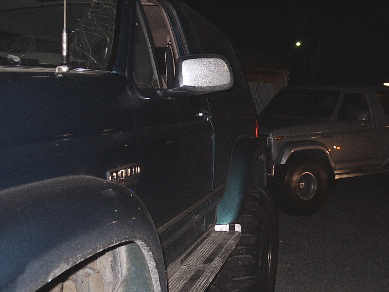 Dark blue Ford Bronco driver side at night beside a lighter SUV