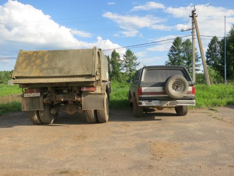1987 Ford Bronco - A 1987 Ford Bronco is parked next to a large truck on a dirt road under a cloudy sky.