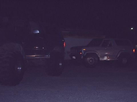 1996 Ford Bronco - Two SUVs are parked side-by-side at night, one is a classic Ford Bronco.