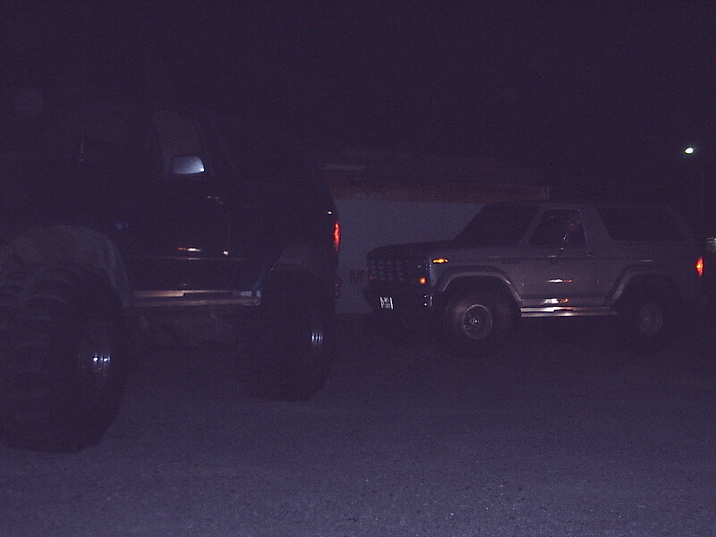 Two Ford Broncos parked at night, one dark and lifted, one light-colored