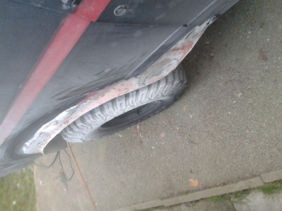 Close-up of a vehicle's lower body panel with rust and a tire visible