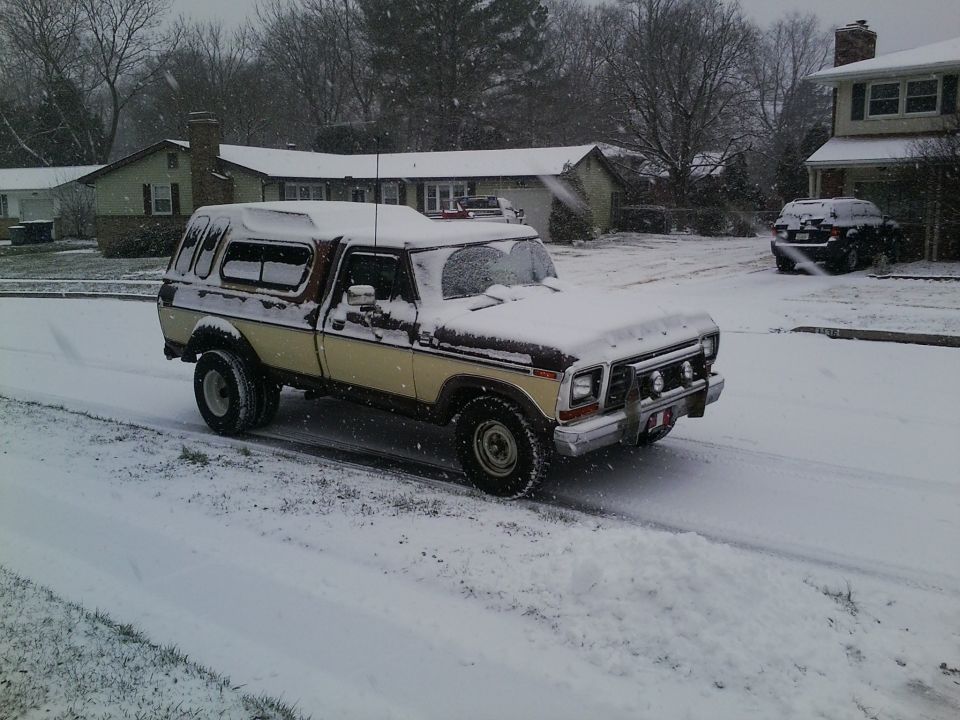 1978 Ford Bronco with camper shell driving in snow, another SUV visible in background