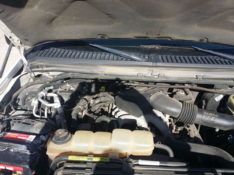 2001 Ford Excursion engine bay with hood open, showing V10 engine components, battery, and coolant reservoir