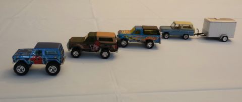 1995 Ford Bronco - A collection of toy trucks, including a blue one with red accents and a blue one with flames, are lined up on a white surface.