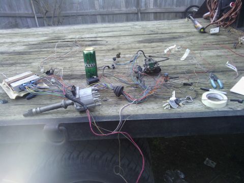 1978 Ford Bronco - A collection of automotive parts, including a wiring harness and distributor, are spread out on a trailer, alongside a can of beer and tool…