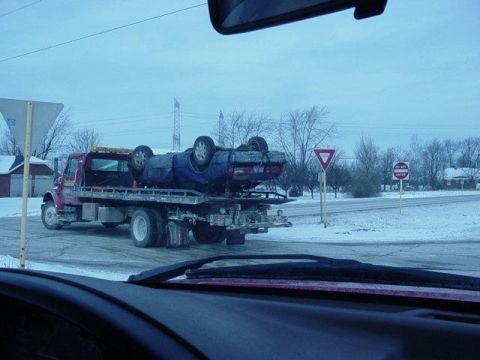 1992 Ford Bronco - A tow truck transports an overturned blue car on a flatbed during a snowy day.