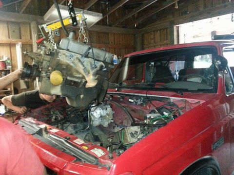 1995 Ford Bronco - Mechanics are working on installing an engine into a red truck in a garage.
