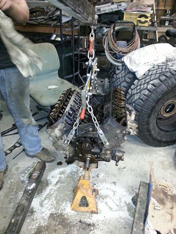 1995 Ford Bronco - An engine is suspended by chains and a hoist, undergoing a rebuild process in a garage setting.