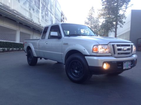 2010 Ford Ranger - Silver pickup truck with black wheels parked in front of a modern building.