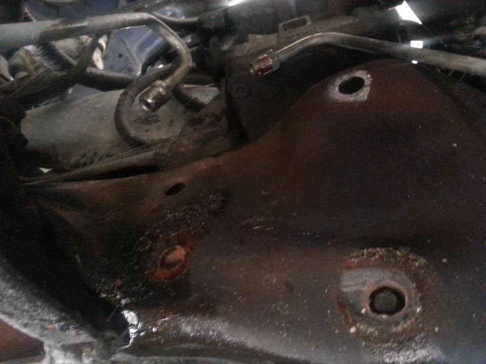 Close-up of a rusty vehicle steering box with hydraulic lines attached