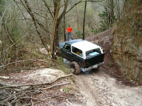 1991 Ford Bronco - A Ford Bronco navigates a challenging off-road trail with a person on its roof.