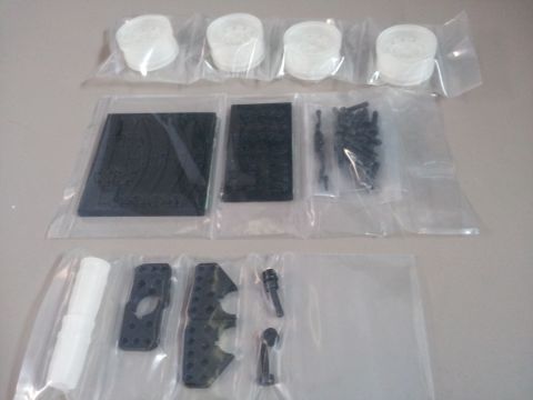 1995 Ford Bronco - Various unassembled parts for a model vehicle, including wheels, black chassis components, and hardware, are displayed in plastic packaging.