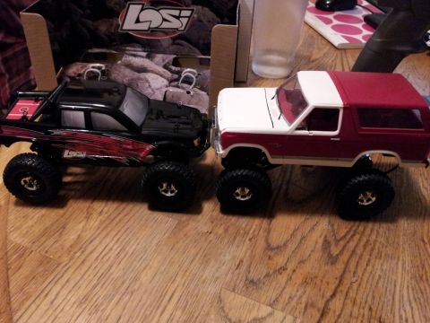 1995 Ford Bronco - Two remote control monster trucks are displayed on a wooden surface, with a box in the background.