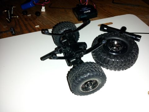 1995 Ford Bronco - RC car chassis and wheels are laid out on a white surface with other small parts.