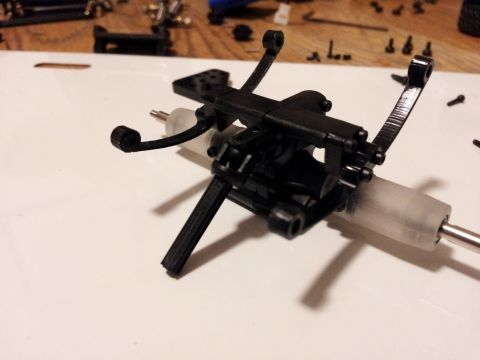 1995 Ford Bronco - Close-up of a black plastic RC car suspension assembly with metal shafts.