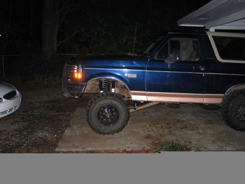 1995 Ford Bronco - A blue Ford Bronco with a tan stripe is shown with a lift kit and large tires.