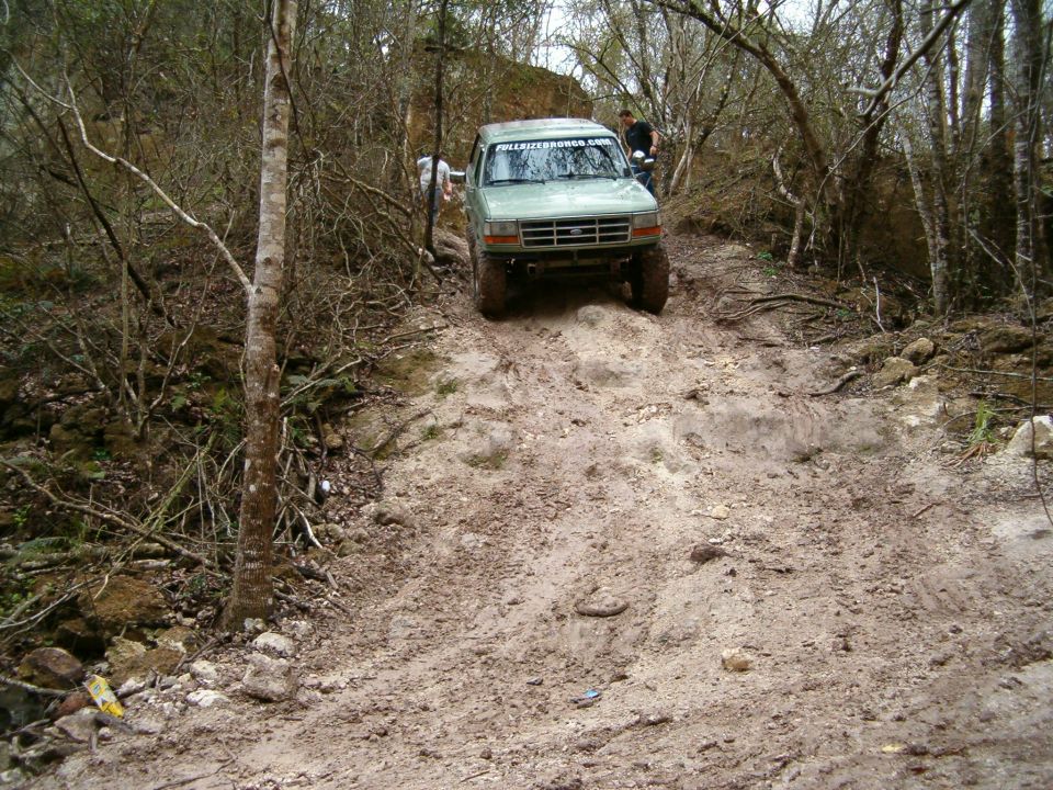 Green Ford Bronco climbing a dirt hill, text on windshield reads 'FULLSIZEBRONCO.COM'