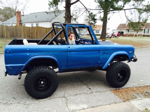 1974 Ford Bronco - A blue 1974 Ford Bronco with a roll cage and off-road tires is parked on a street.