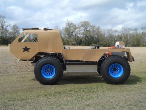 1992 Ford Bronco - A custom-built vehicle with oversized tires and a unique construction sits on a grassy field under a cloudy sky.