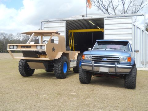 1992 Ford Bronco - A blue Ford pickup truck, likely from the late 1980s, sits beside a unique, unfinished custom vehicle.