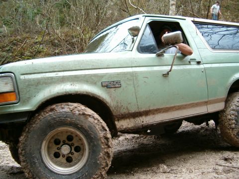 1991 Ford Bronco - A light green Ford Bronco navigates a muddy off-road trail.