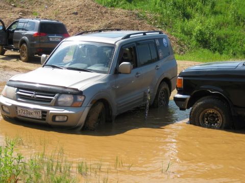 1987 Ford Bronco - Two SUVs, a silver Mitsubishi and a black Ford Bronco, navigate a muddy off-road course.