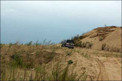 1987 Ford Bronco - 1987 Ford Bronco navigates a sandy incline under a hazy sky.