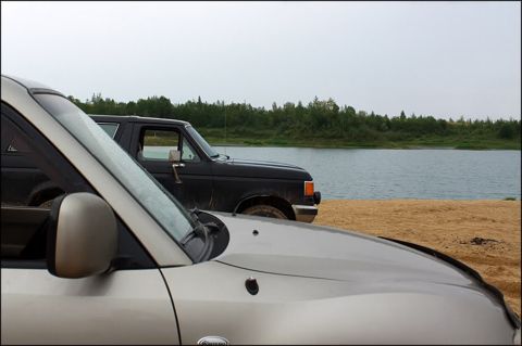 1987 Ford Bronco - A black 1987 Ford Bronco is parked on a sandy shore next to a body of water.